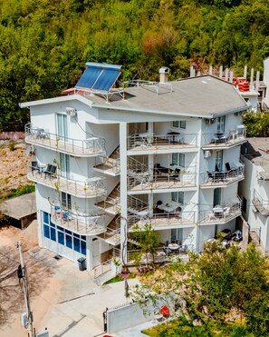 A multi-story building with balconies, solar panels, and outdoor seating. - Apartmani Grbovic (Čanj)