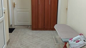 A room with a tiled floor, a wooden wardrobe, a door labeled 'A1', and a table with an ironing board.