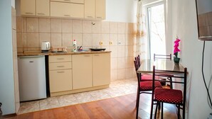 A kitchen with beige cabinets, a refrigerator, a dining table with chairs, and a window with a curtain.