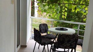 A balcony with a table and chairs, a view of greenery, and a door.