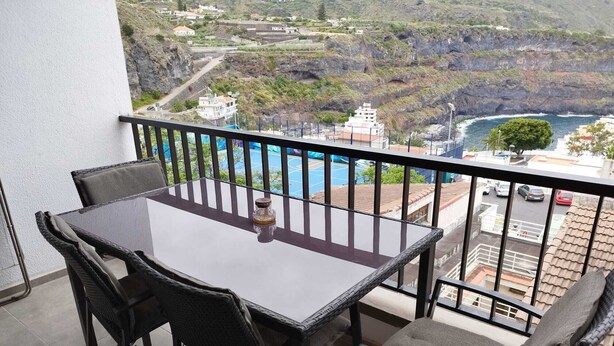 A balcony with a table and chairs, overlooking a coastal landscape with buildings and cliffs. - Apartment with a beautiful view and a balcony (San Marcos)