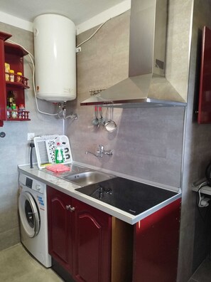 Eine kleine Küche mit integriertem Waschmaschine, Spüle aus Edelstahl und Durchlauferhitzer in Weiß.