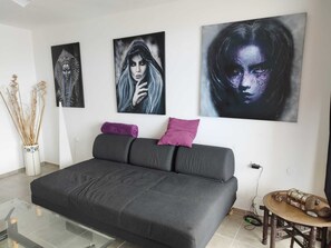 Ein modernes Wohnzimmer mit einem grauen Sofa, zwei violetten Kissen und drei Kunstwerken an der Wand.