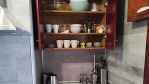 A compact kitchen with a built-in stove, a sink, and a wooden shelf above the countertop holding various dishes and utensils. - Apartment with a beautiful view and a balcony (San Marcos)