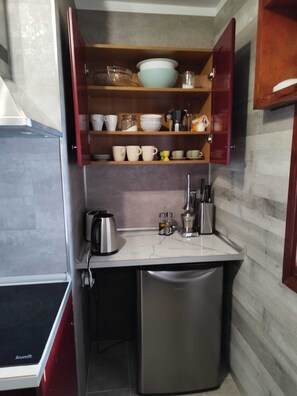 A compact kitchen with a built-in stove, a sink, and a wooden shelf above the countertop holding various dishes and utensils. - Apartment with a beautiful view and a balcony (San Marcos)