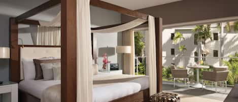 A four-poster bed with a canopy, a bedside table with a lamp, and a view of a balcony with outdoor furniture.