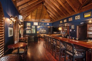 A bar area with wooden ceiling beams, a bar counter, and seating with cushioned chairs.
