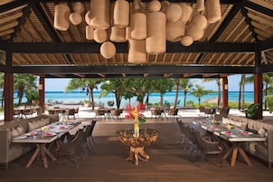 An outdoor dining area with a glass table, wicker hanging lights, and a view of the ocean.