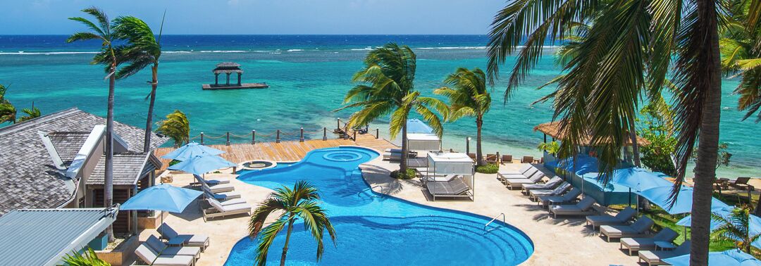 A resort pool area with lounge chairs, umbrellas, and a view of the ocean.