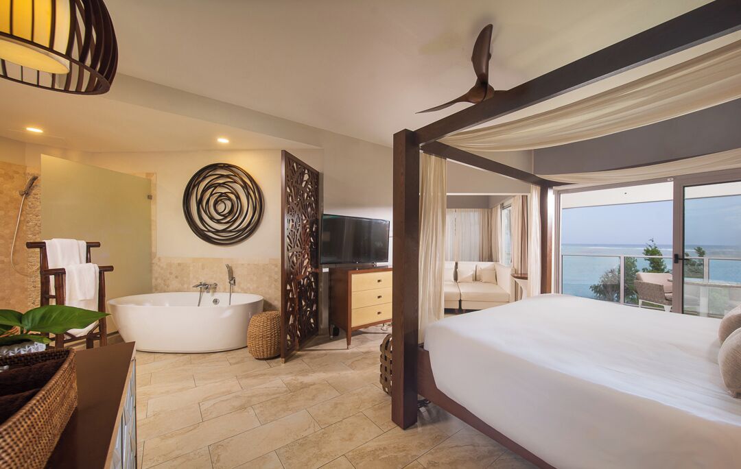 Un dormitorio moderno con una cama grande, una bañera y un balcón con vista al mar.