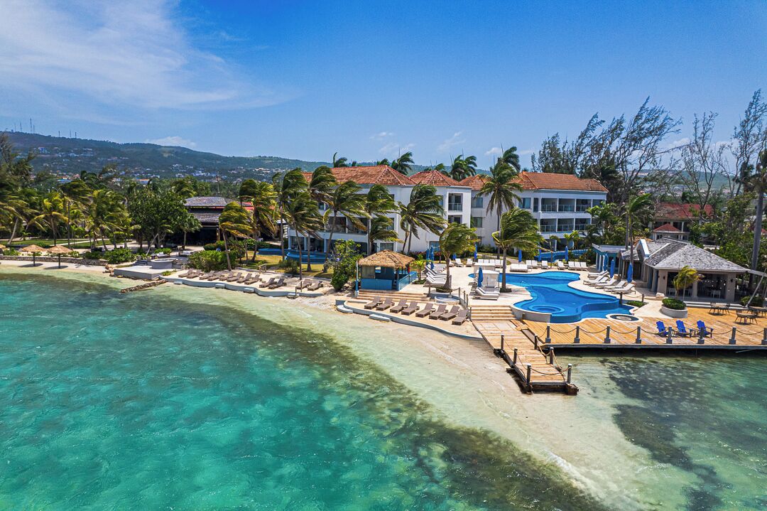 A resort with a swimming pool, beach, and palm trees.