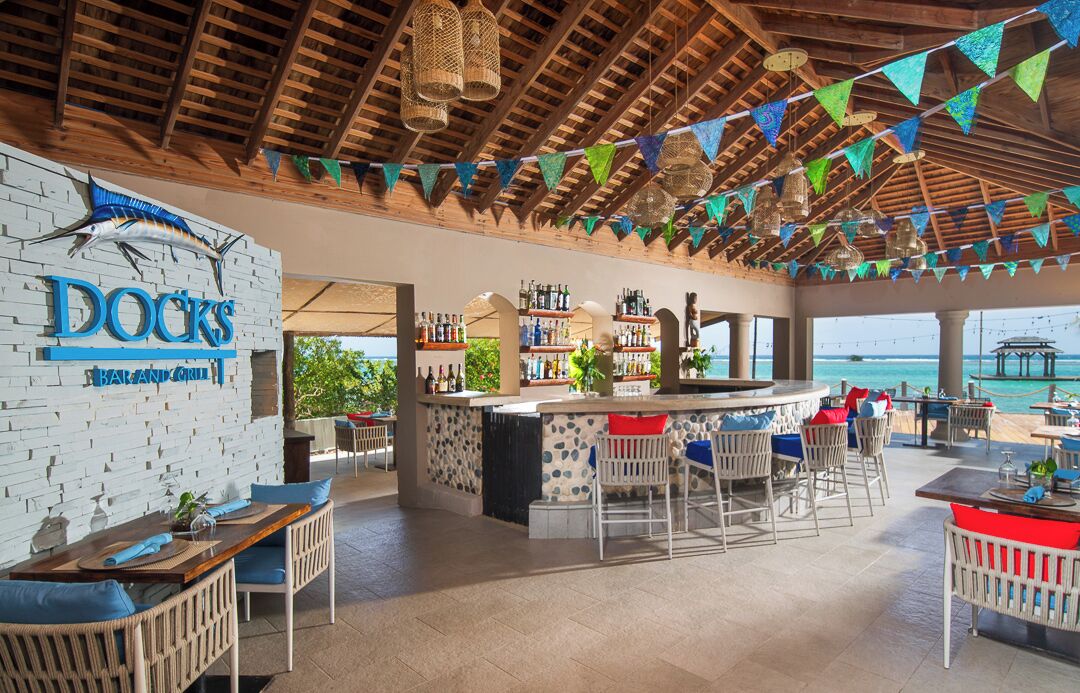 Zona de bar con techo de madera, taburetes y vista al mar.