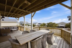 A covered outdoor deck with a wooden table and wicker chairs, overlooking a residential street. - Steps from Beach with Ocean Views and Fresh Updates (Oak Island)