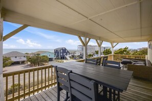 A covered outdoor deck with a table and chairs, overlooking a residential area and the ocean. - Steps from Beach with Ocean Views and Fresh Updates (Oak Island)