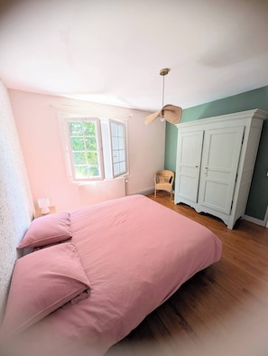 Un dormitorio con cama, una silla, un armario y ventana.