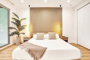 A modern bedroom with a large bed, a bedside plant, and a wooden headboard. - Las Olas-8 BD with Two HTD Pool-Jacuzzi-BBQ-Games (Fort Lauderdale)