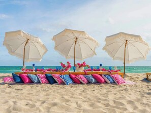 A beach setting with three umbrellas, a table with pink and blue patterned cushions, and a floral arrangement. - HTD Pool-Jacuzzi-BBQ-Games-Near Las Olas 1 (Fort Lauderdale)