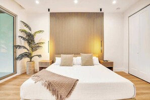 Ein modernes Schlafzimmer mit einem großen Bett, einer Topfpflanze und einem Holzkopfende.