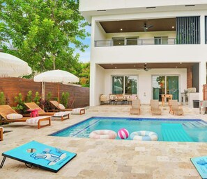 Ein modernes, zweistöckiges Haus mit Schwimmbad, Außenmöbeln und einer überdachten Terrasse.