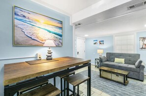 Ein Wohnzimmer mit einem Holztisch, einem grauen Sofa und einem Bild von einer Strandlandschaft.