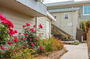 Ein Wohngebäude mit überdachter Veranda, einer Treppe und einem Garten mit rosa Blüten.