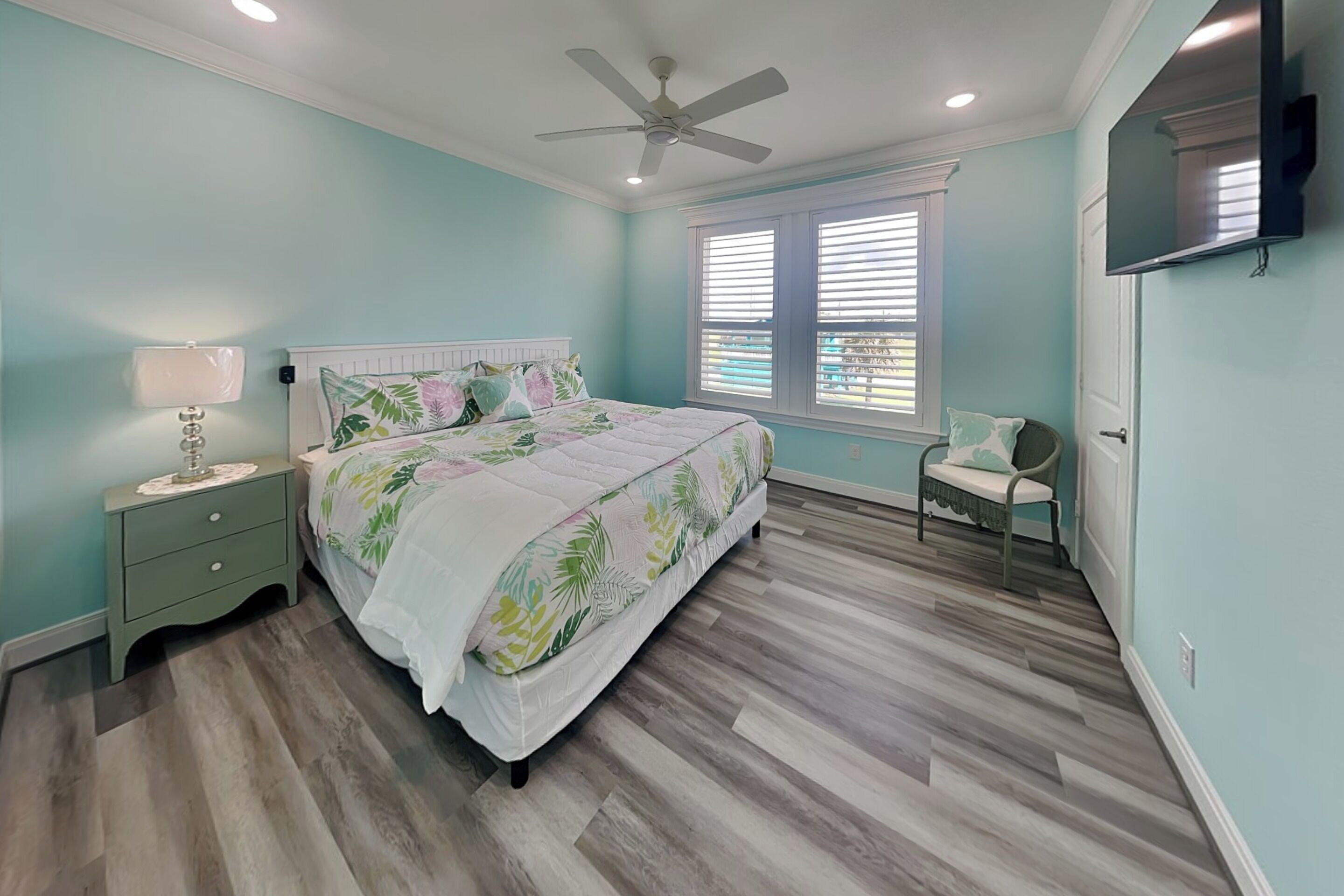 A bedroom with a bed, nightstand, lamp, chair, window, and ceiling fan.