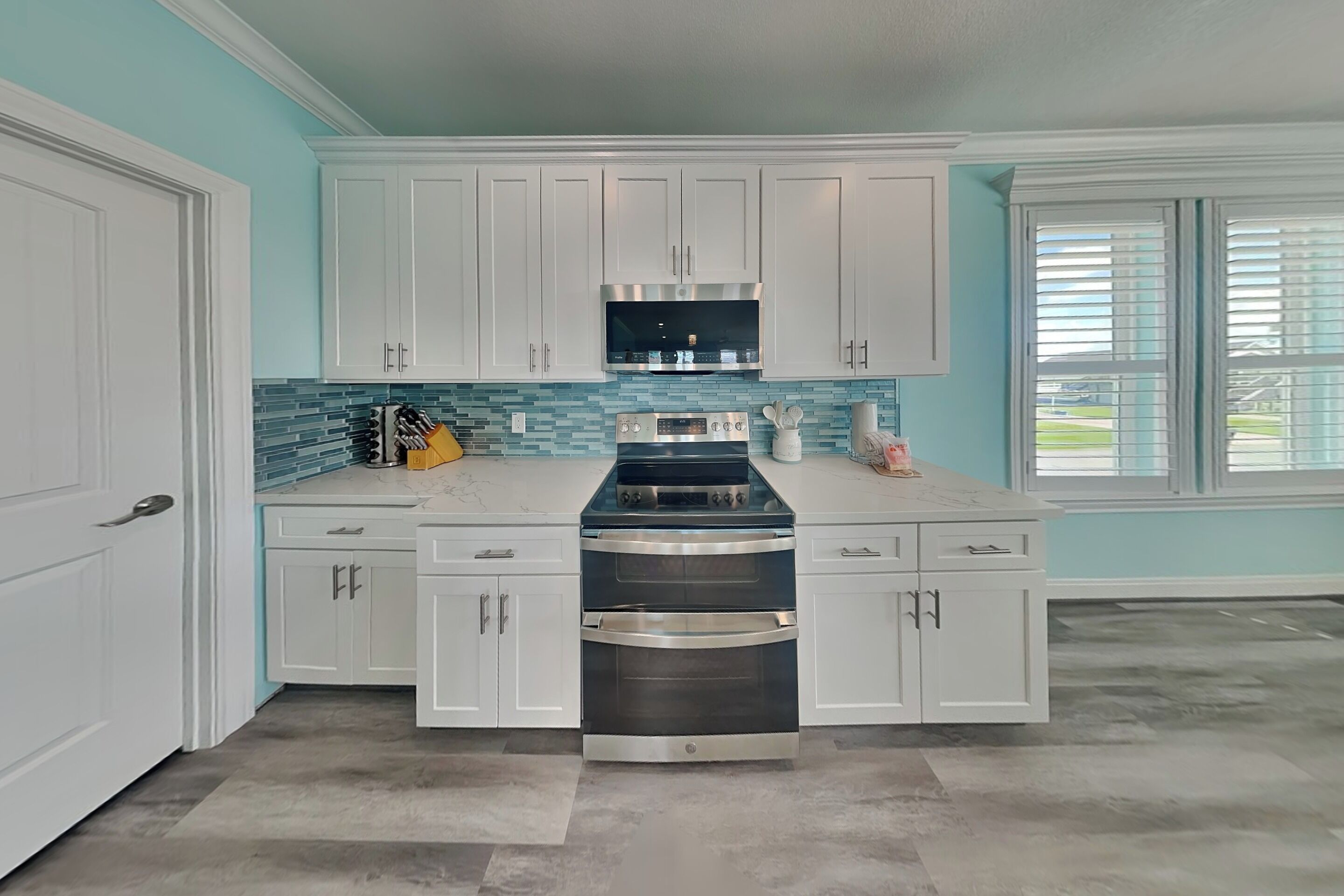 A kitchen with white cabinets, a stainless steel oven, and a backsplash with blue tiles.