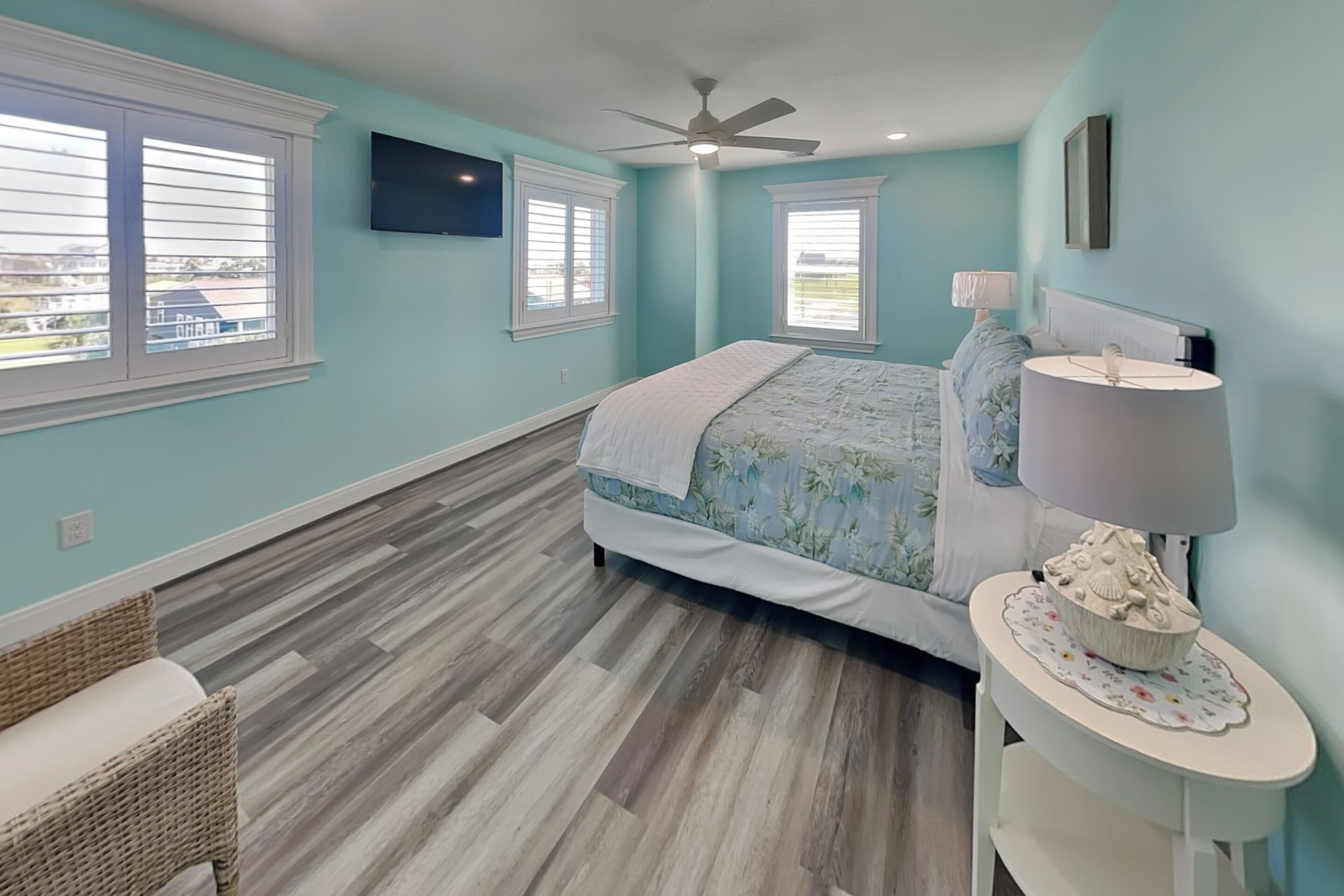 A bedroom with a bed, a ceiling fan, a TV, a lamp, and a window.