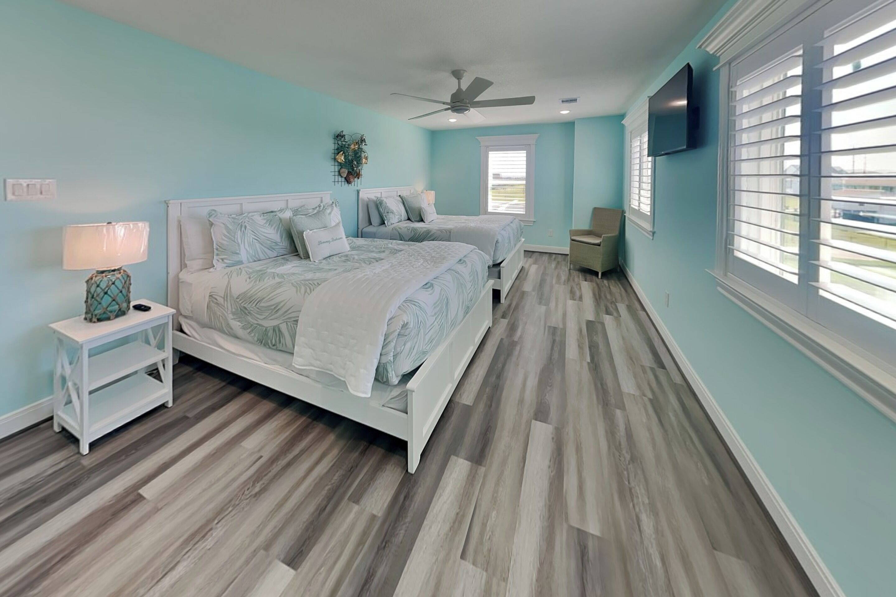 Une chambre avec deux lits, un ventilateur de plafond, une télévision et une fenêtre avec des stores.