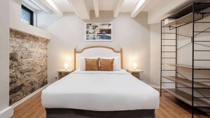 A bedroom with a large bed, stone wall, wooden headboard, two bedside lamps, and a framed picture on the wall. - Comfort Queen – Montreal Stay (Montréal)