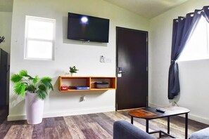 Ein Wohnzimmer mit Fernseher, einer Tür, einer kleinen Pflanze, einem Bücherregal und einem Tisch.