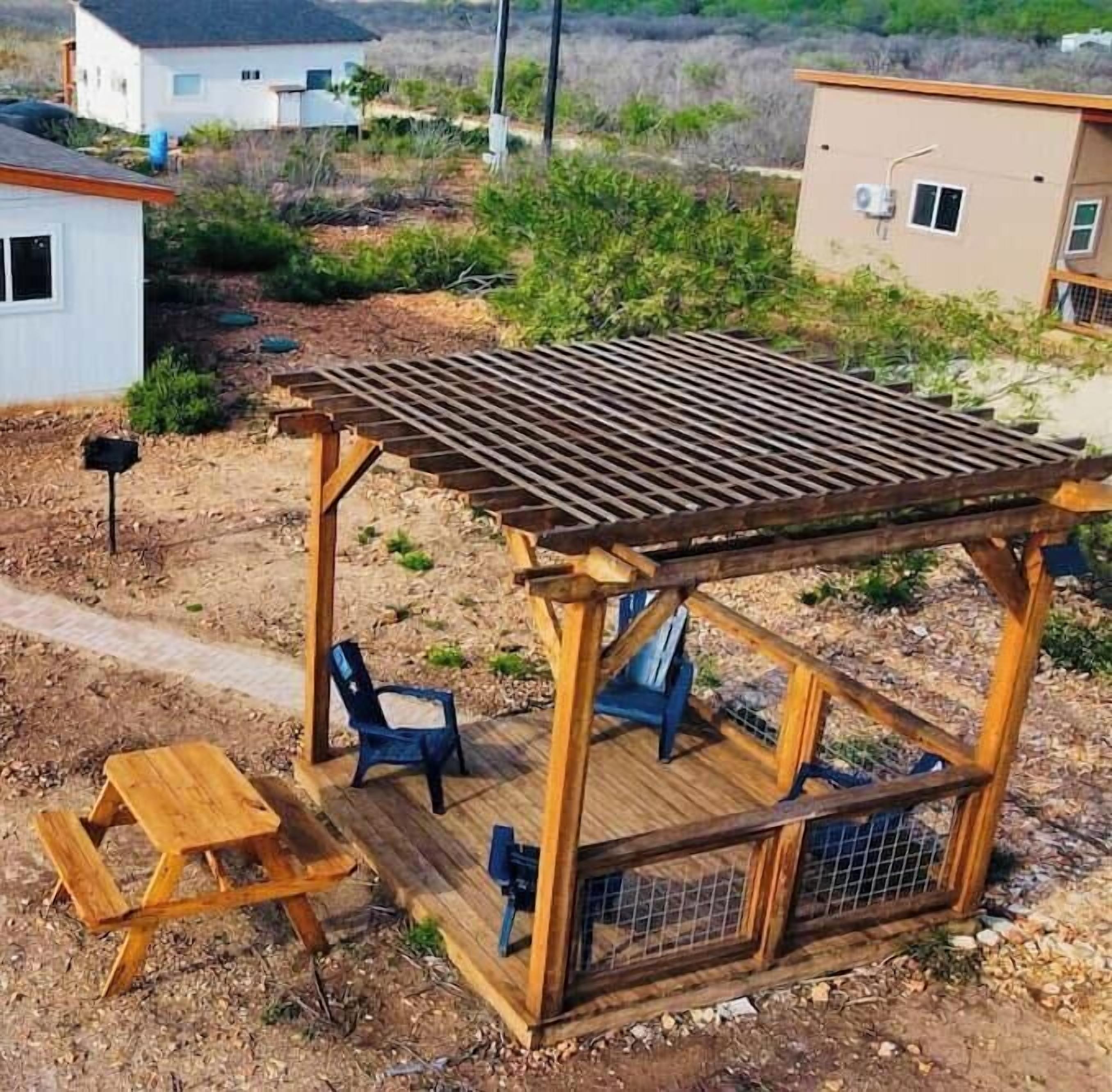 Puuinen pergola, jossa on pöytä ja tuoleja.