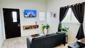 Ein Wohnzimmer mit einer Couch, Fernseher, Topfpflanzen und einem Fenster mit Vorhängen.