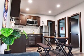 A modern kitchen with dark wooden cabinets, stainless steel appliances, and a dining area with a bench. - 22 Eleven Claystone cozy cabin BBQ grill, Firepit, Pergola (Devine)