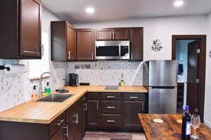 A modern kitchen with dark wooden cabinets, stainless steel appliances, and a wooden countertop. - 22 Eleven Claystone cozy cabin BBQ grill, Firepit, Pergola (Devine)