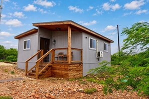 A small, single-story cabin with a wooden staircase leading to a porch, a small porch area, and a window on the side. - 22 Eleven Claystone cozy cabin BBQ grill, Firepit, Pergola (Devine)
