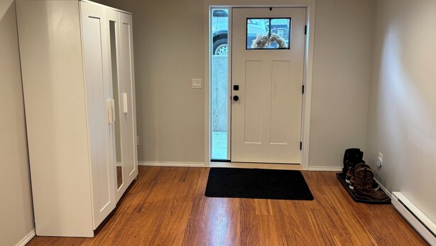 A hallway with a white door, a black mat, and a pair of boots. -        Salmon Arm Comfortable 2 Bedroom in town, 5 minute drive to the beach! (Salmon Arm)