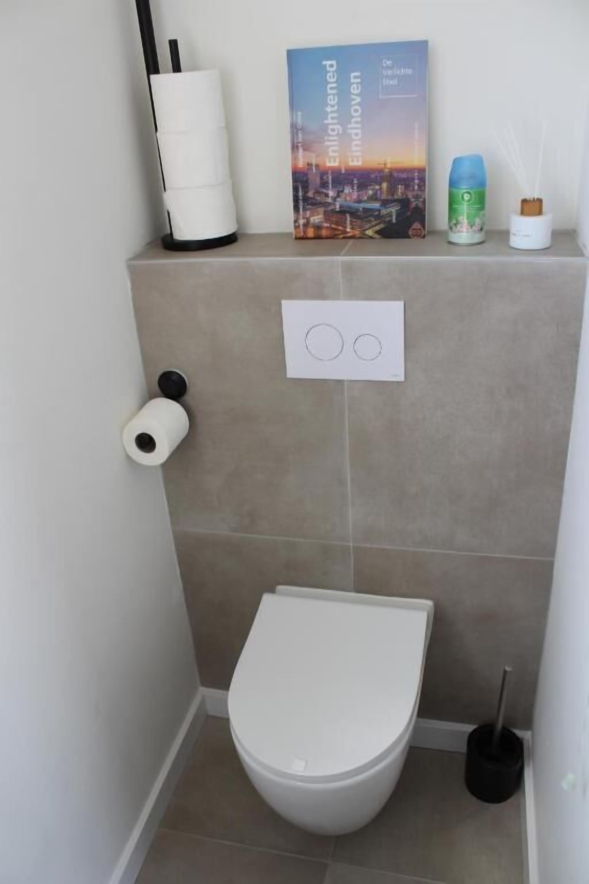 Un bagno piccolo con un water, un portasciugamani per carta igienica, un libro e un asciugamani ad aria.
