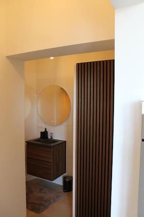 A modern bathroom with a wooden vanity, a round mirror, and a dark floor rug.