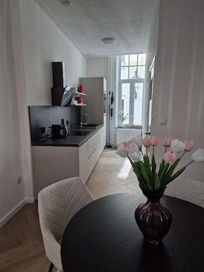 A modern kitchen with white cabinets, a black countertop, and a vase of pink tulips on a round table.