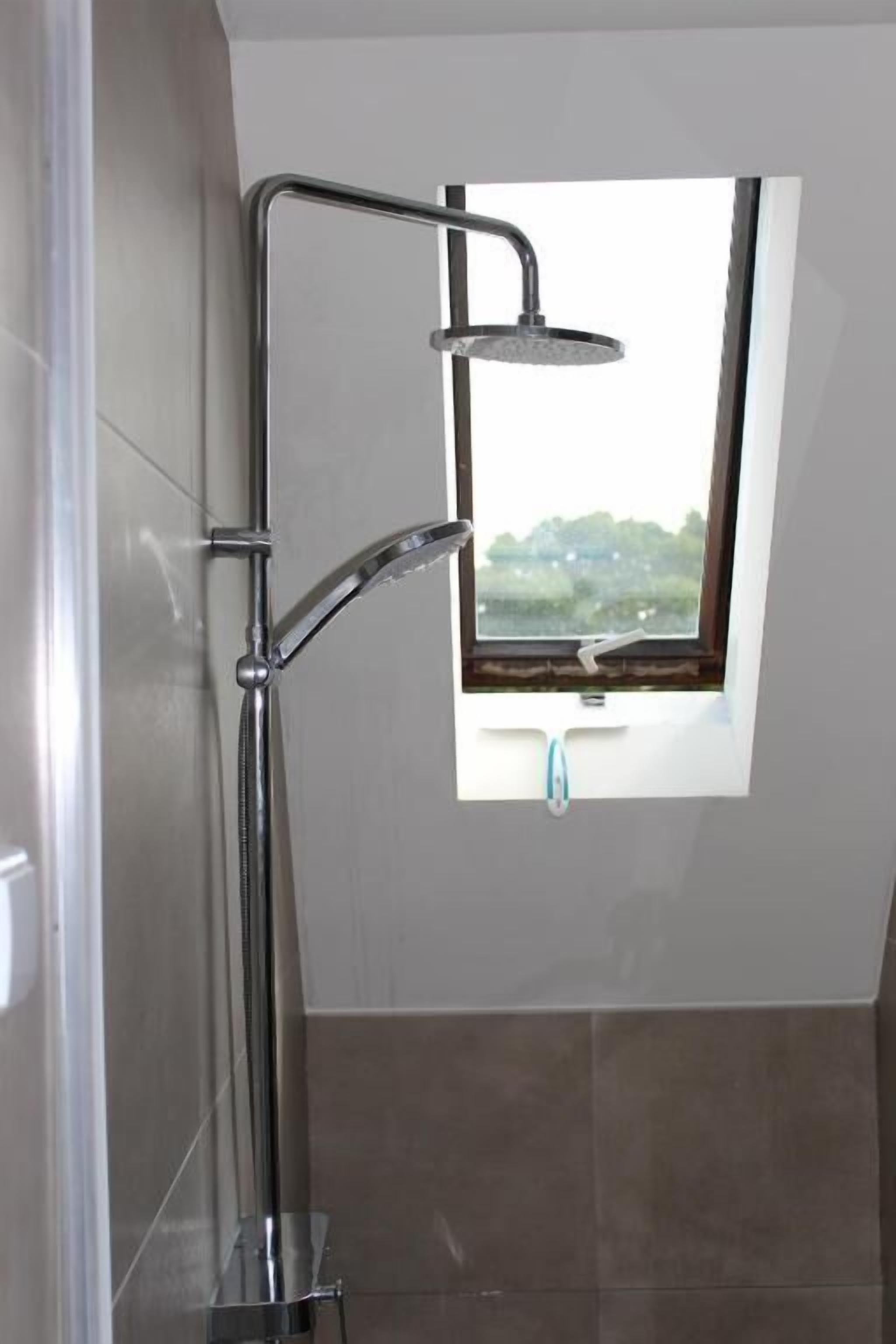 A shower with a window, a view of greenery outside, and a tiled wall.