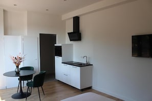 A compact kitchen with a sink, cabinets, and a black range hood. There is a dining area with a table and chairs. - Studio & Apartments Roermond (Roermond)