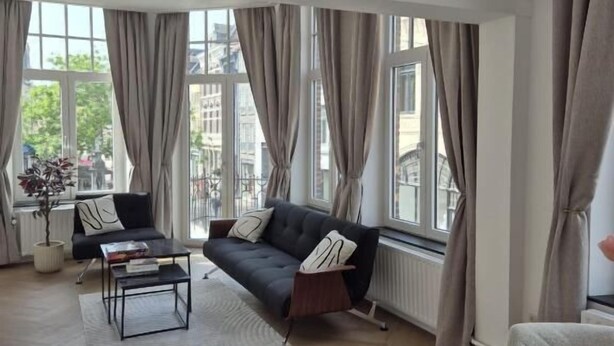 A spacious living room with a sofa, coffee table, and large windows with curtains. - Studio & Apartments Roermond (Roermond)