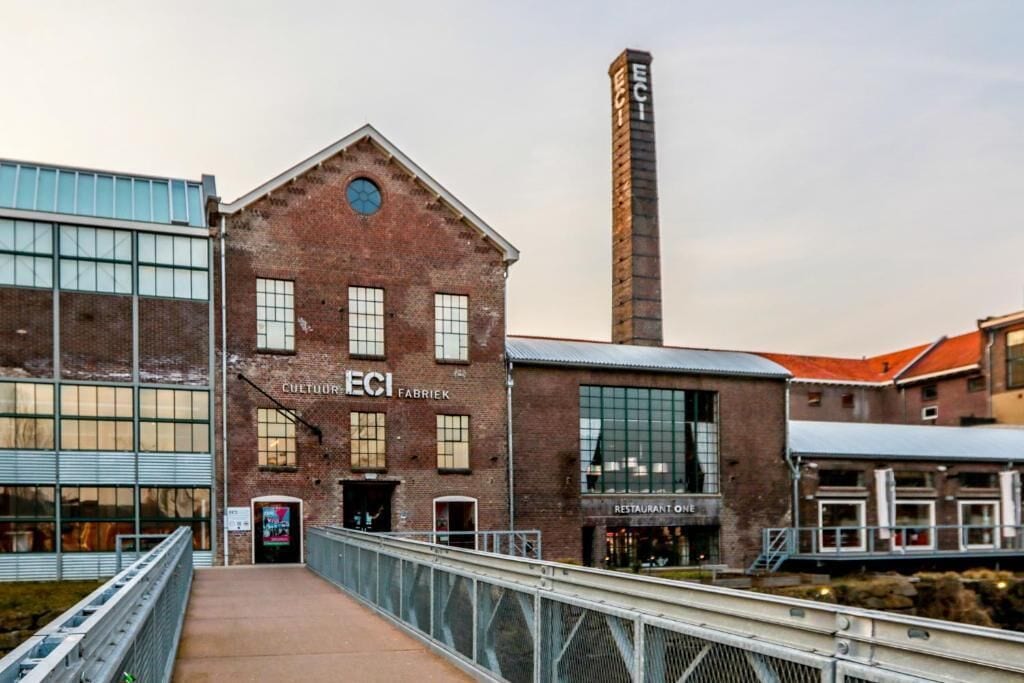 A brick building with large windows and a tall chimney, labeled 'ECI FABRIK' and 'RESTAURANT ONE'.