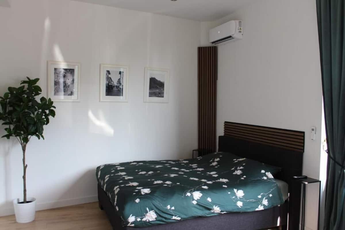 A bedroom with a bed, a potted plant, and three framed pictures on the wall.