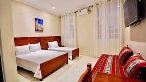 Une chambre dâhĂŽtel avec deux lits simples, un canapĂ©, un tableau et une tĂ©lĂ©vision.