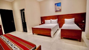 A hotel room with two beds, a wooden headboard, a painting on the wall, and a red patterned tablecloth.