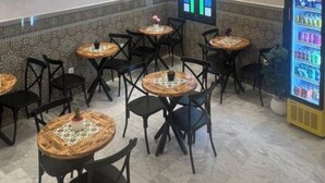 Un restaurante con mesas redondas, sillas negras, una araña de cristal, un televisor y una máquina expendedora.