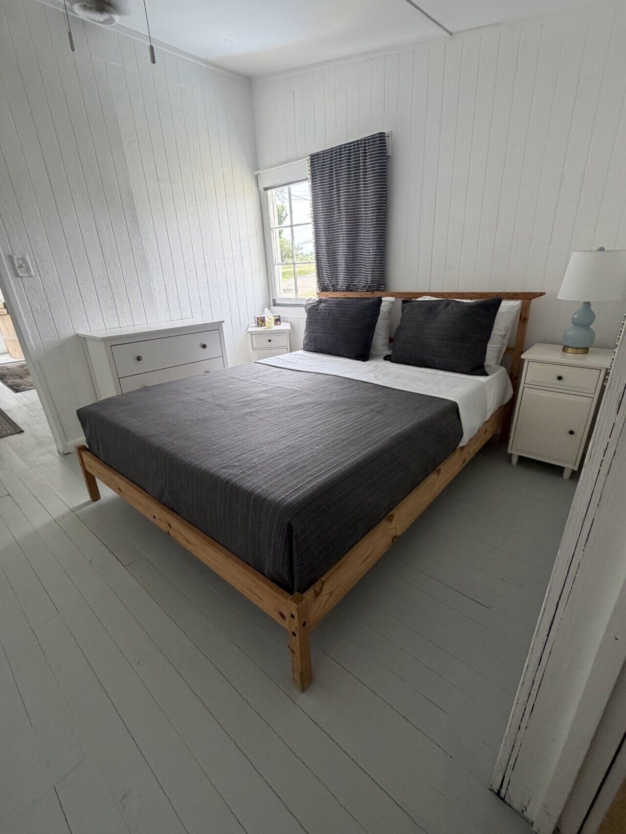 A bedroom with a large bed, a nightstand, a bedside table, a window with blinds, and a ceiling fan.. Plum Point Cottage #17
