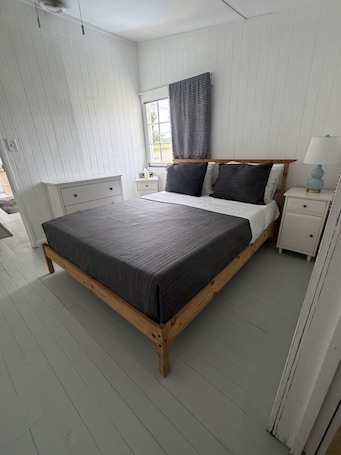 A bedroom with a large bed, a nightstand, a bedside table, a window with blinds, and a ceiling fan.. Plum Point Cottage #17
